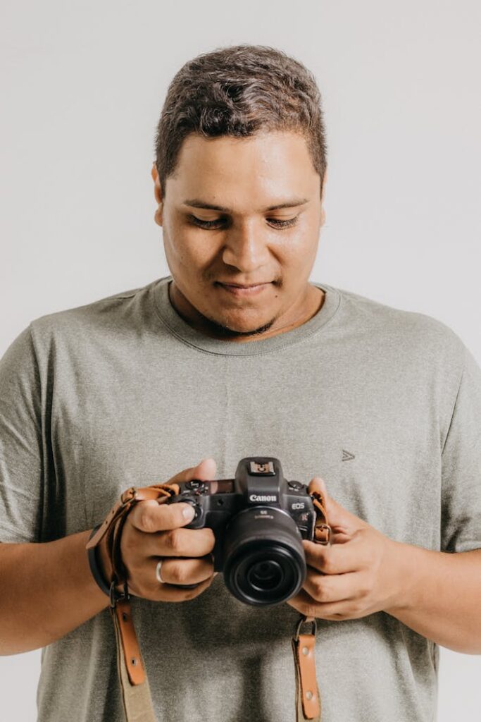 Man with short hair holding Canon camera, inspecting settings in a studio setup.